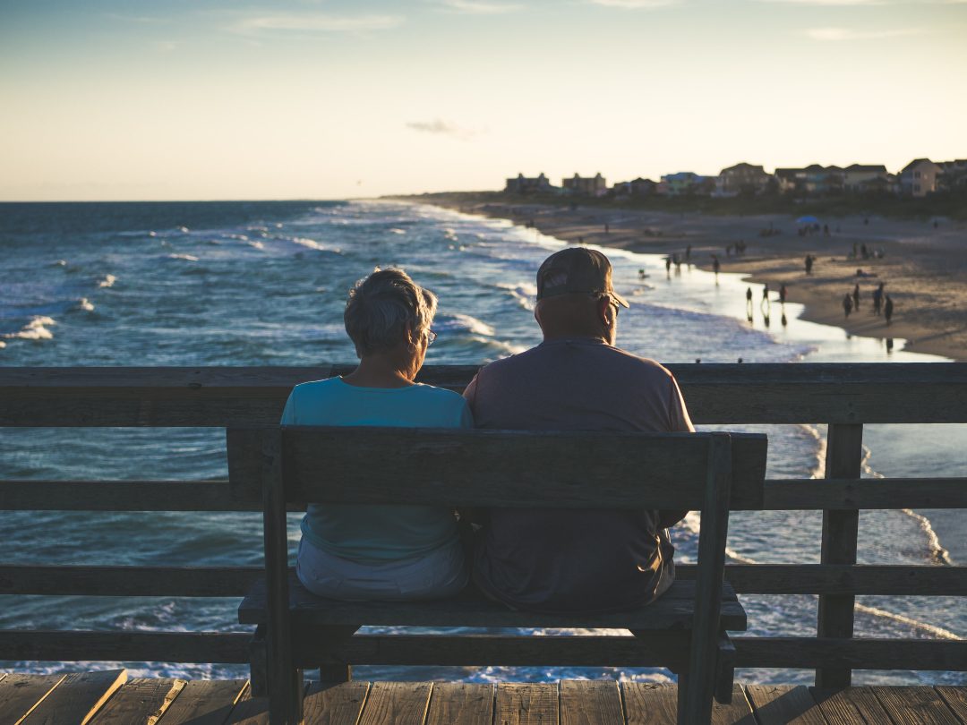 Older couple sitting on a beach pier bench looking at the ocean_sell_your_house_fast_and_retire_portland_oregon